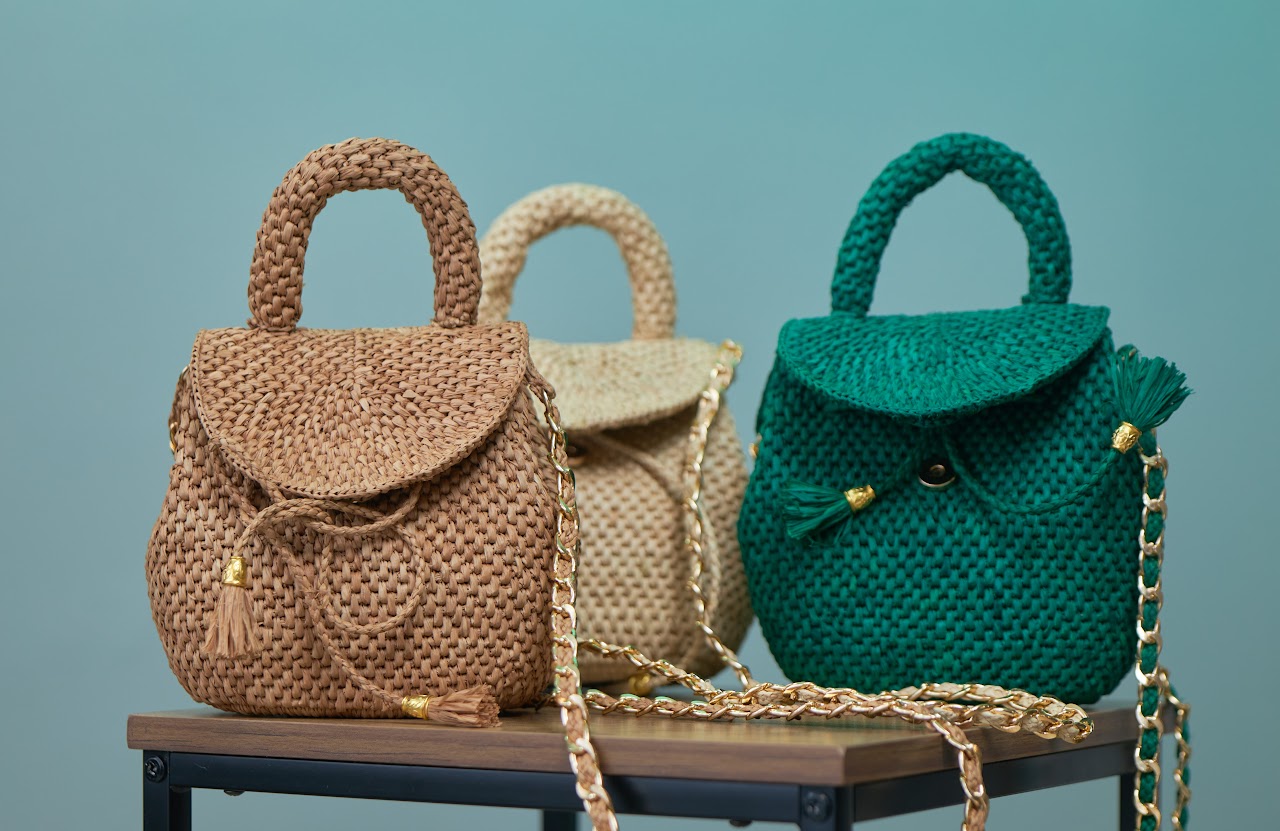 Three handcrafted raffia handbags in natural, ivory and emerald tones